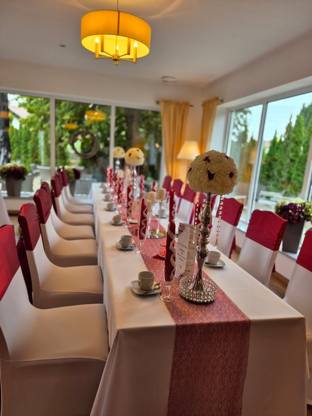Lange Festtafel mit roten Stühlen, rosé Läufer und Rosenkugeln