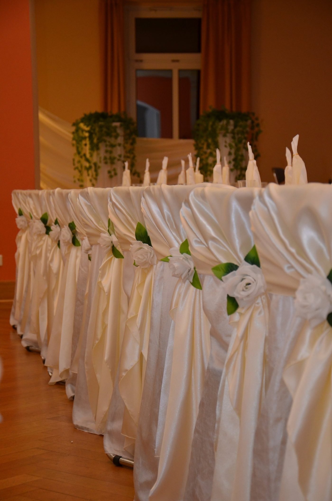 Weiße Stretchhussen mit Satin-Schleifen und Rosen auf Hochzeitsstühlen
