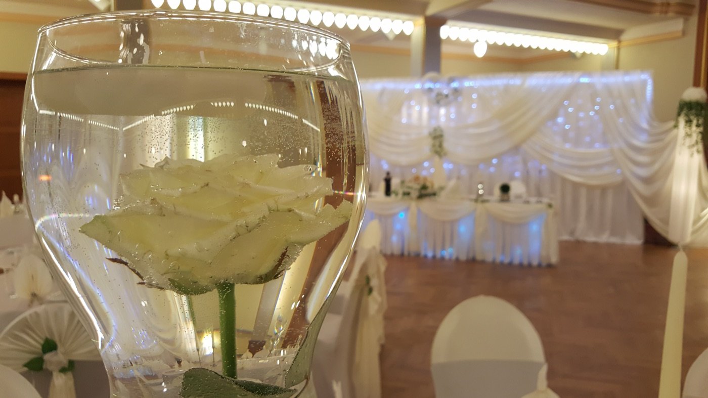 Weiße Rose in der Glasvase vor dem cremefarbenen Festsaal