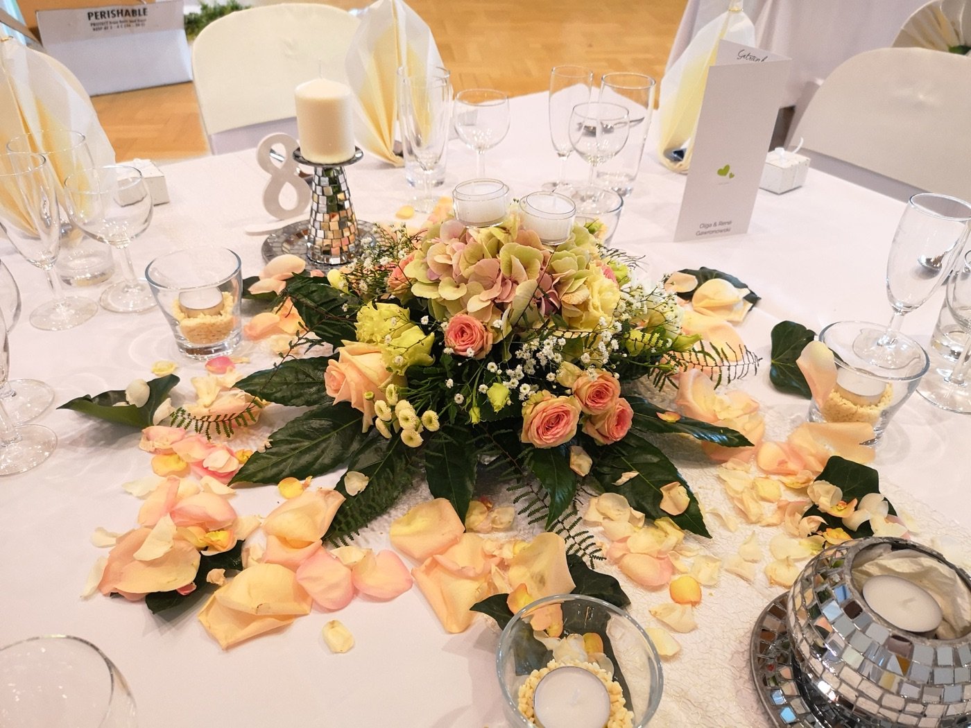Apricotfarbenes Blumengesteck mit Rosenblättern auf der Festtafel