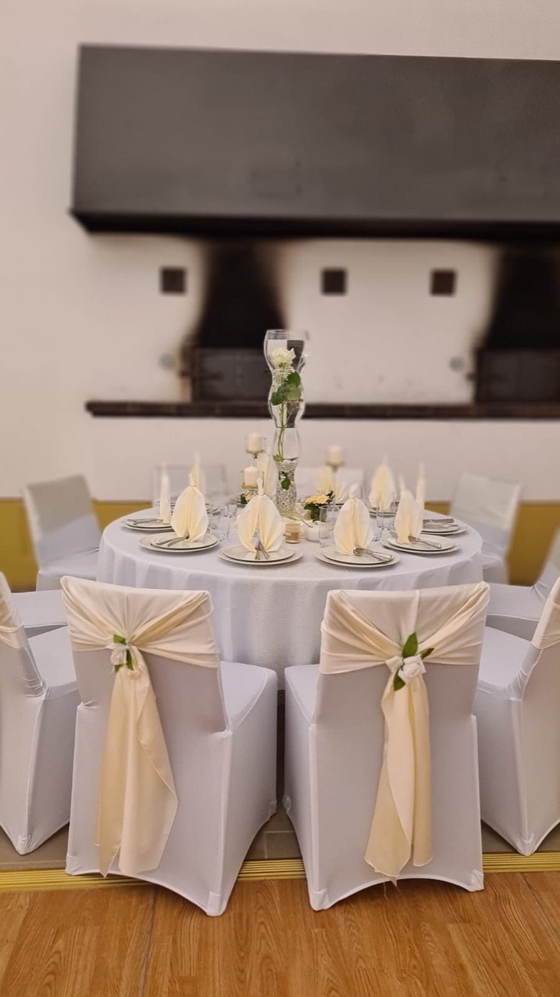 Runder Tisch mit weißen Stuhlhussen, Champagner-Schleifen und hoher Vase
