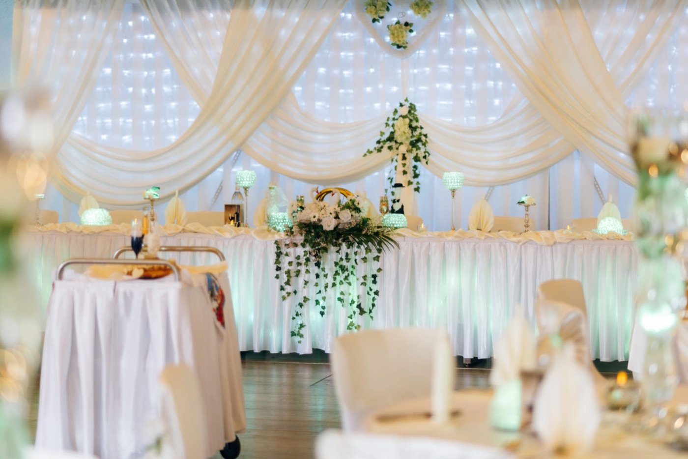 Eleganter Festsaal mit cremefarbenem Stoffhimmel, Lichtern und Blumenbogen