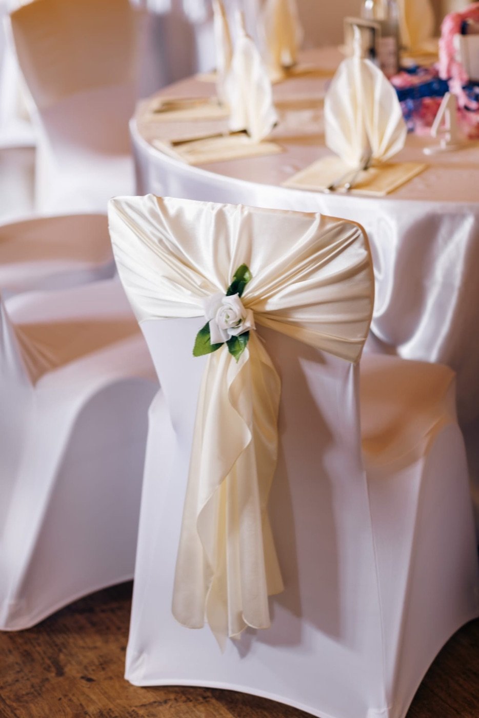 Stuhlhusse mit champagnerfarbener Satinschleife und weißer Rose, elegantes Detail