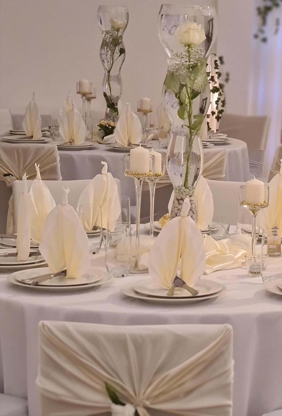 Festtafeln in Creme mit hohen Rosen-Vasen und gefächerten Servietten