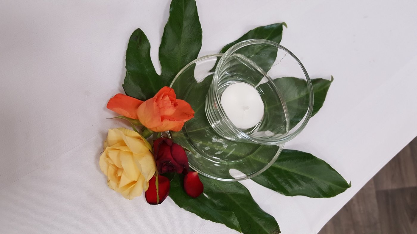 Schwimmkerze im Glas mit Rosen und grünem Blatt als Tischdeko-Detail