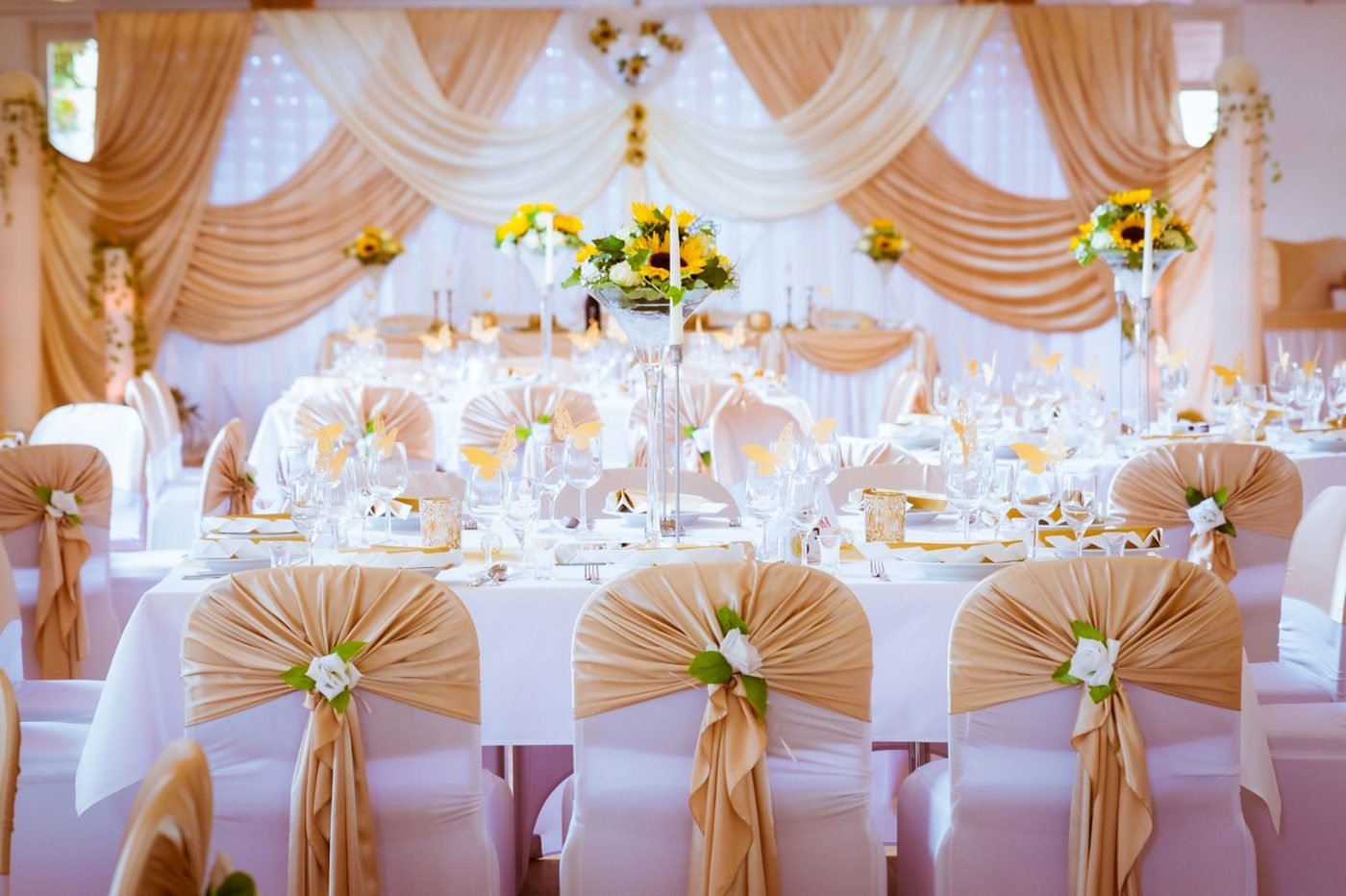 Hochzeitssaal in Gold mit drapiertem Stoffhimmel, Sonnenblumen und goldenen Stuhlschleifen