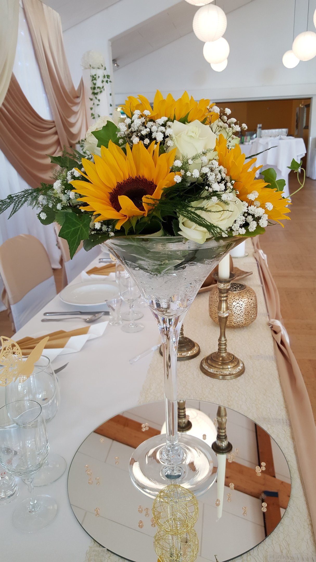 Hohe Martini-Vase mit Sonnenblumen-Gesteck auf der Hochzeitstafel in Gold