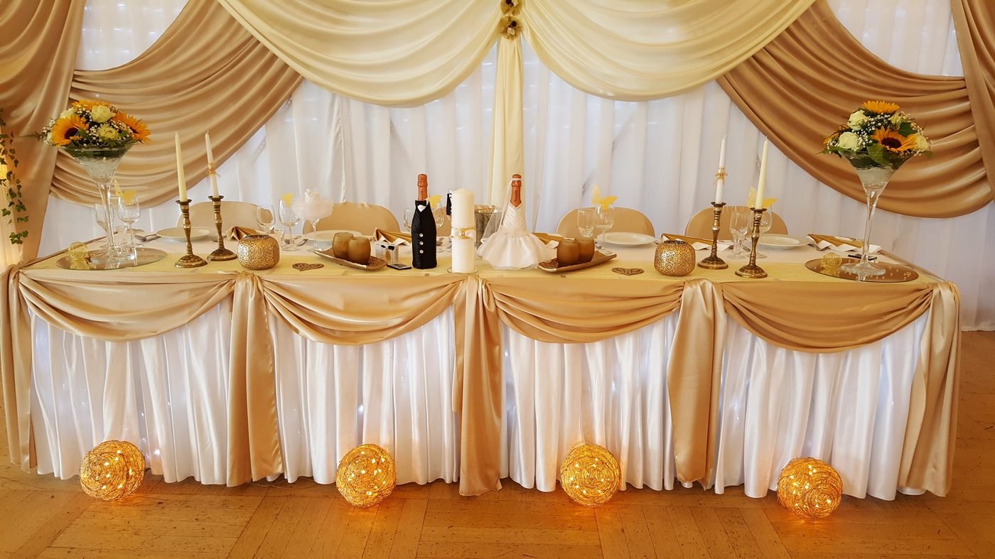 Brauttisch mit goldener Stoffdrapierung, Kerzen und leuchtenden Rosenkugeln