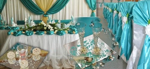 Brauttisch in Türkis und Gold mit Blumengestecken und dekorierten Gläsern