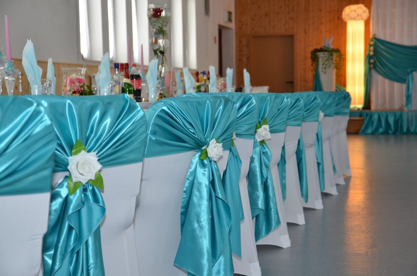 Gemietete Stuhlhussen mit türkisen Satin-Schleifen und weißen Rosen